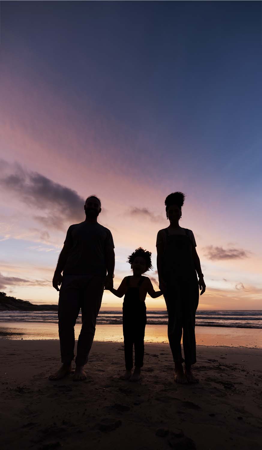 Silhouette of two adults holding hands with a child at sunset