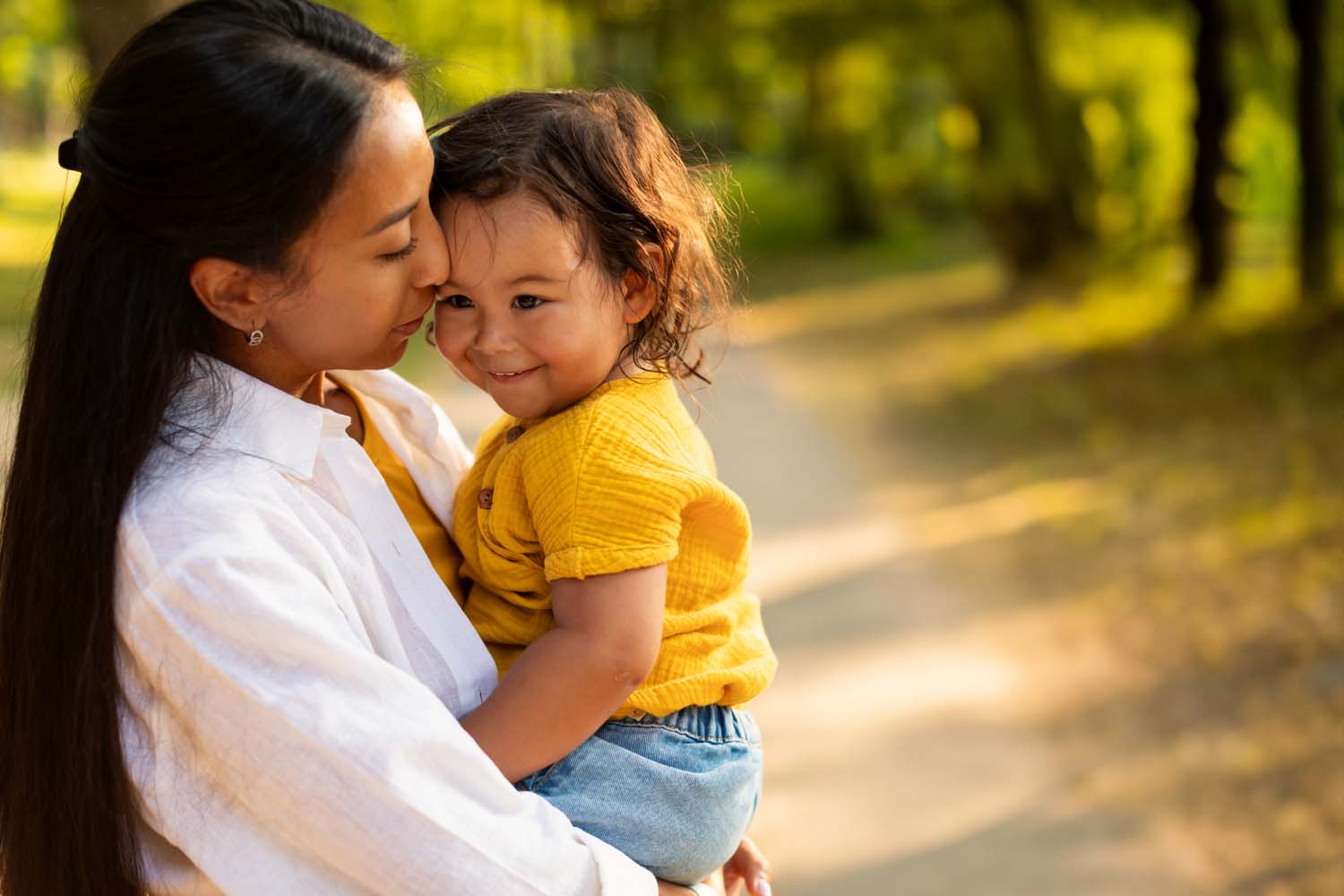 Mother holding her smiling young child close on a sunlit path